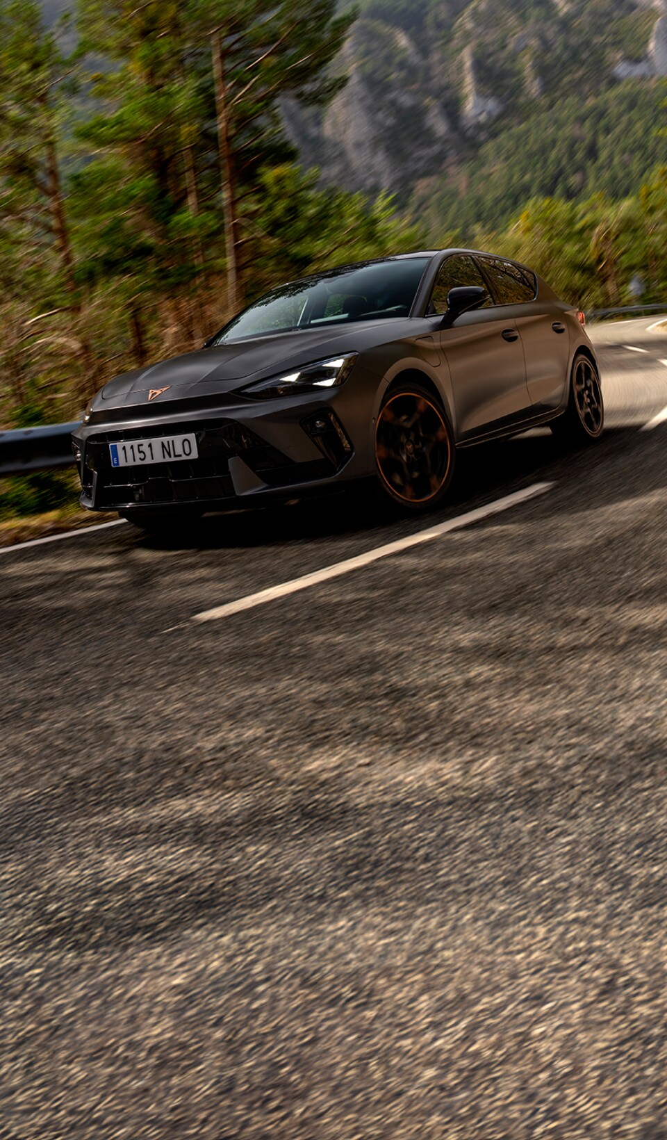 A CUPRA Leon hatchback seen from an elevated angle with its headlights on, next to a person covered in dark, flowing fabric that drapes onto the ground.