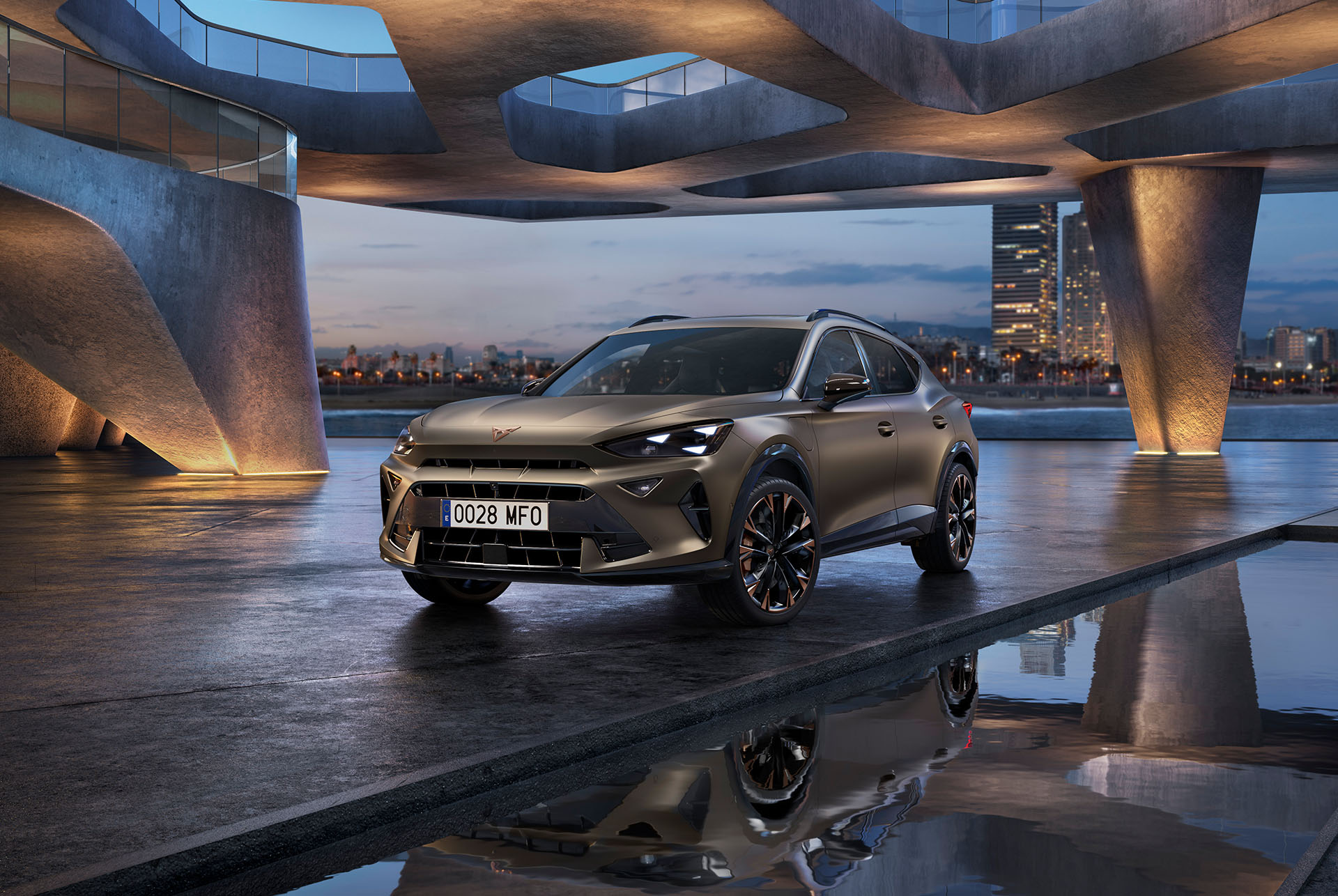 UPRA Formentor kerevärviga Century Bronze Matt, pargitud peegeldava veepinnaga piirnevale promenaadile. Sportlik ja aerodünaamiline uus sõiduk on paigutatud keskkaadrisse. Auto on ümbritsetud futuristlikust arhitektuurist, taustal paistab õhtuhämaruses helendav Barcelona siluett.